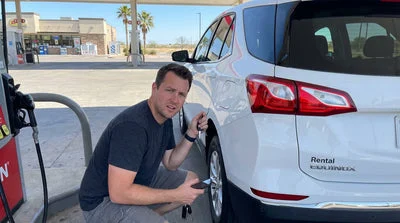 A driver stands by their car rental at a gas station in Texas, looking at the locking fuel cap