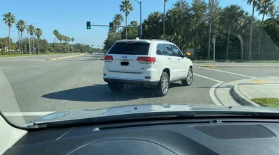 A car hire vehicle stopped at a traffic light on a sunny Florida road with a right-turn slip lane ahead